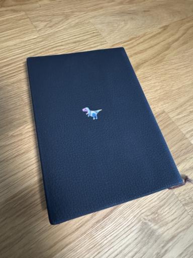A black book with a textured cover, featuring a small, colorful dinosaur design on the front.