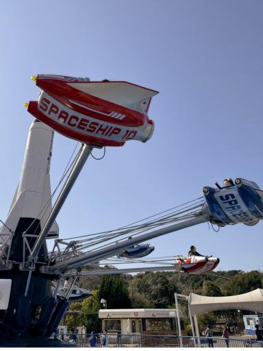 People are enjoying a spinning amusement park ride designed like spaceships. The ride has multiple colorful cars, with